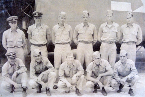 Officers in Navy uniforms stand on the deck of a ship. 